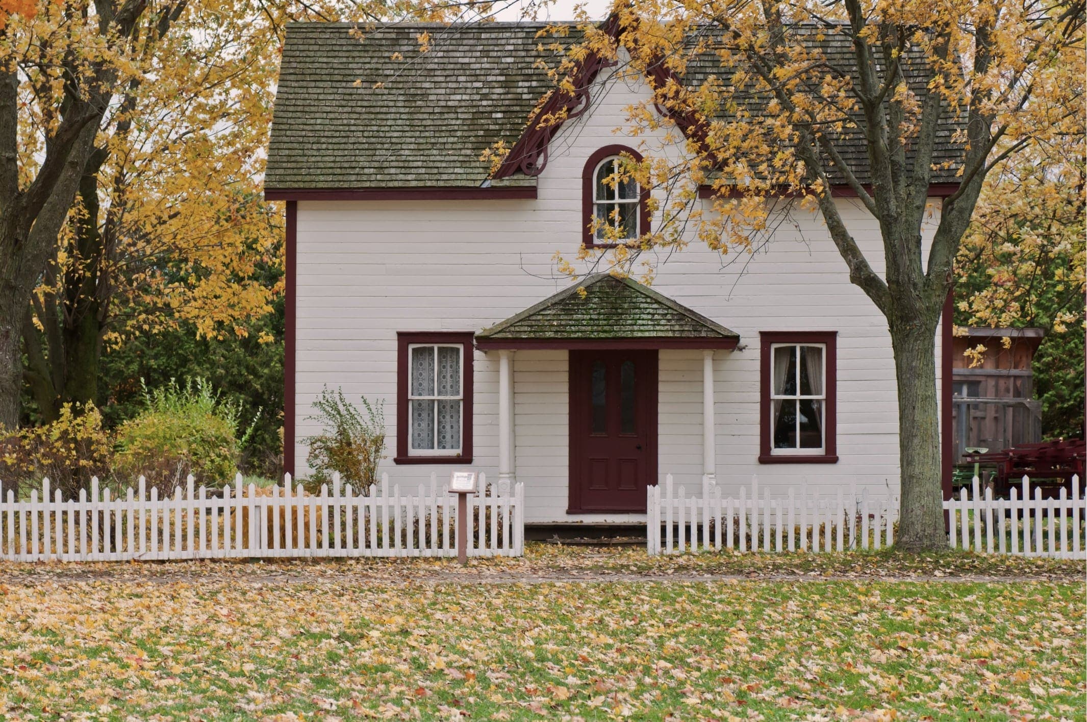 Compact detached cottage home with a covered entry porch and white picket fence