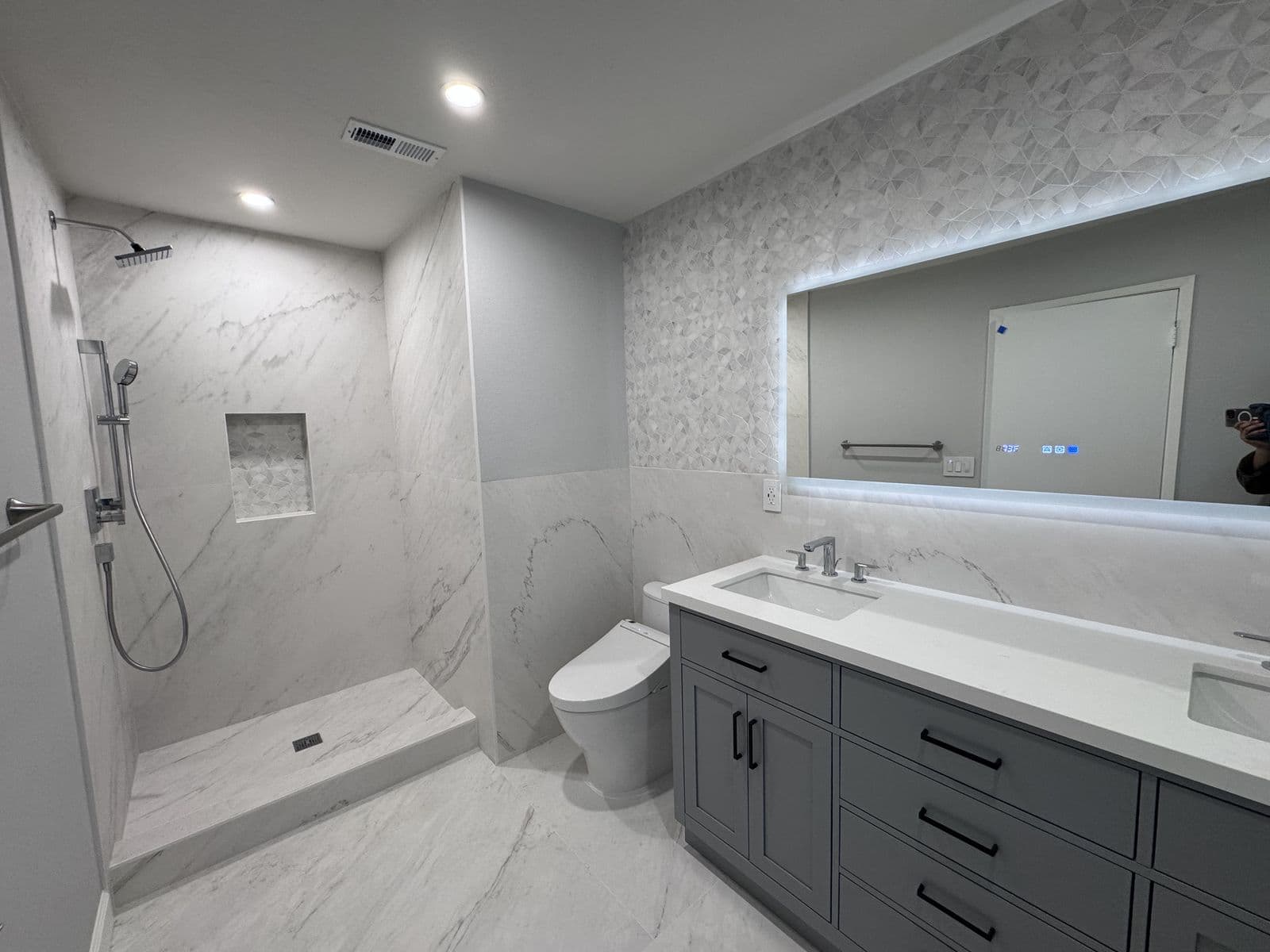 Bathroom remodel with a double grey vanity, marble-look walk-in shower, and backlit LED mirror