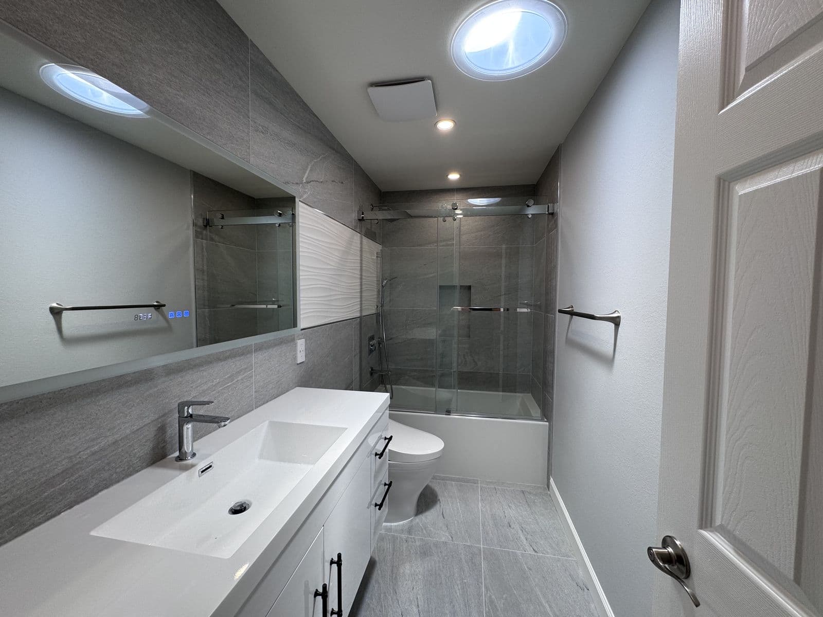 Bathroom remodel with large-format grey porcelain tile and a floating trough-sink vanity