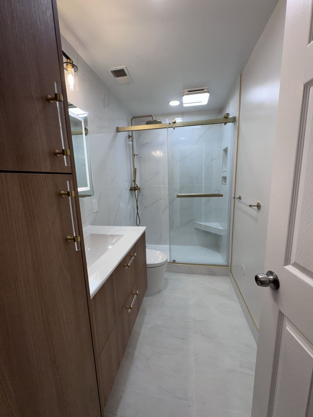 Bathroom remodel with a floating oak vanity, brushed-brass fixtures, and a glass shower